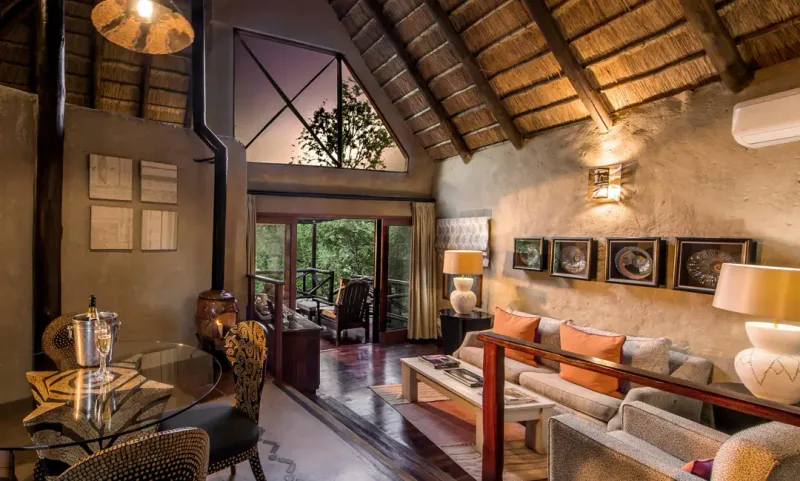 Warmly lit luxury bush lodge suite with thatched roof and African decor